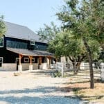 Black metal barndominium building with white trim among oak trees