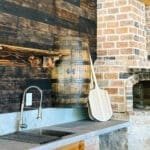 Whiskey barrel beside a stone fireplace at an outdoor kitchen