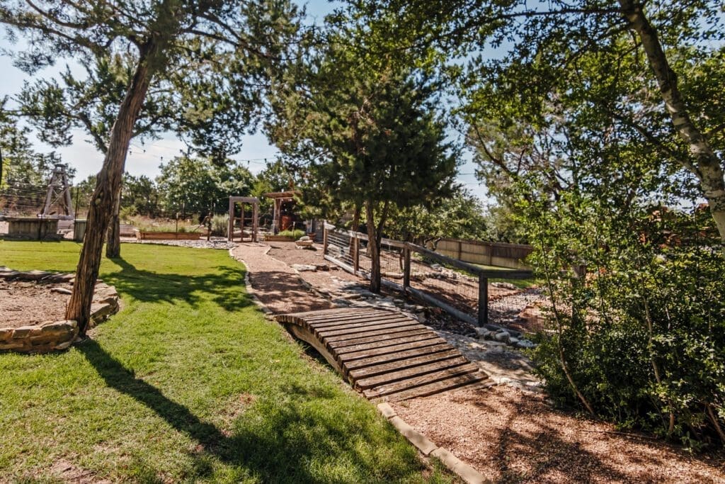 Custom home outdoor wooden bridge and water feature landscaping in Dripping Springs TX