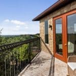 Covered balcony with iron railing and Hill Country views at a custom stone home