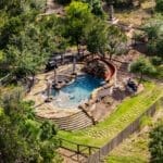 Aerial view of a rock pool and spa in a tree-shaded Dripping Springs backyard