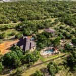 Aerial view of a custom home with backyard pool tucked among Hill Country oaks